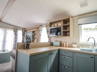 A kitchen with blue cabinets a microwave a sink and a knife set at Burlees Nest in Brigham near Great Broughton Cockermouth