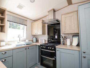 A kitchen with blue lower cabinets and wooden upper cabinets a black oven a silver extractor fan and utensils on the counter at Burlees Nest Brigham near Great Broughton Cockermouth