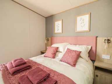 A bedroom with a bed with pink cushions and folded towels at Burlees Nest in Brigham near Great Broughton Cockermouth