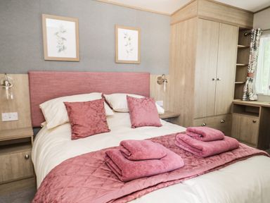 A bedroom with a double bed pink cushions pink towels wooden cabinets and a window at Burlees Nest in Brigham near Great Broughton Cockermouth