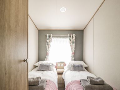 A bedroom with two single beds and a window with patterned curtains at Burlees Nest in Brigham near Great Broughton Cockermouth