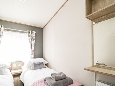 A small bedroom with two single beds a window with curtains and a wooden vanity with a mirror at Burlees Nest in Brigham near Great Broughton Cockermouth