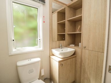 A bathroom with a toilet and a sink with wooden cabinets and shelves at Burlees Nest in Brigham near Great Broughton Cockermouth