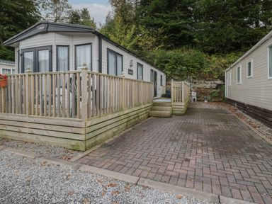 An exterior view of a mobile home with a wooden deck and paved driveway at Burlees Nest in Brigham near Great Broughton Cockermouth