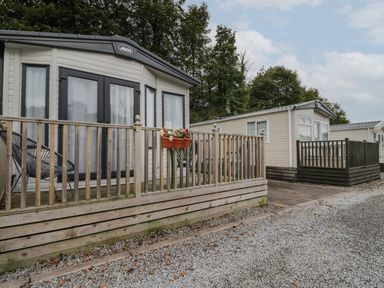 Two caravans with wooden decking and railing on a gravel path with trees in the background at Burlees Nest in Brigham near Great Broughton Cockermouth