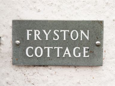 A stone plaque with the words Fryston Cottage mounted on a white textured wall at Fryston Cottage in Keswick