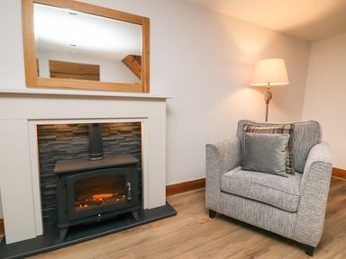 A fireplace with a mirror above and a gray armchair with cushions next to a floor lamp at Fryston Cottage in Keswick