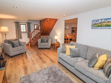 A living room with two armchairs a sofa with pillows a wooden staircase and a dining area at Fryston Cottage in Keswick