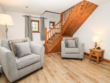 A sitting area with two armchairs a wooden staircase and a side table with a lamp at Fryston Cottage in Keswick