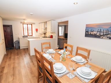 A dining table set with white dishes and glasses in a kitchen with wooden floor and cabinets at Fryston Cottage in Keswick