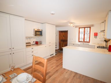 A kitchen with white cabinets wooden flooring and a dining table at Fryston Cottage in Keswick