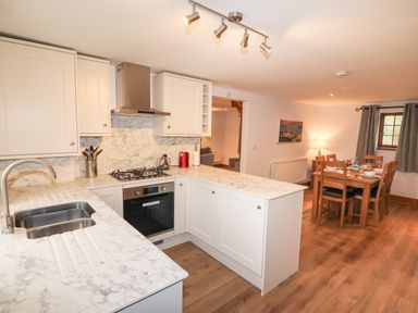 A kitchen with white marble countertops and cabinets next to a dining area with a wooden table and chairs at Fryston Cottage in Keswick