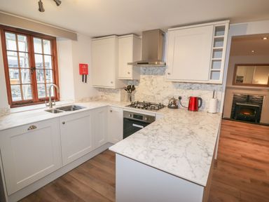 A kitchen with marble countertops, white cabinets, a window with wooden frame, and cooking appliances at Fryston Cottage in Keswick