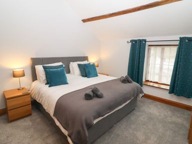 A bedroom with a bed with white sheets and blue pillows two bedside tables with lamps and a window with blue curtains at Fryston Cottage in Keswick