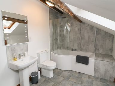 A bathroom with a sink toilet and bathtub under a sloped ceiling at Fryston Cottage in Keswick