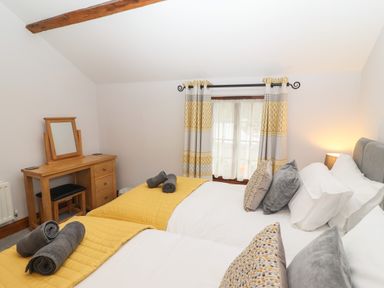 A bedroom with two single beds with yellow throws and grey towels a wooden dressing table with a mirror and patterned curtains at Fryston Cottage in Keswick