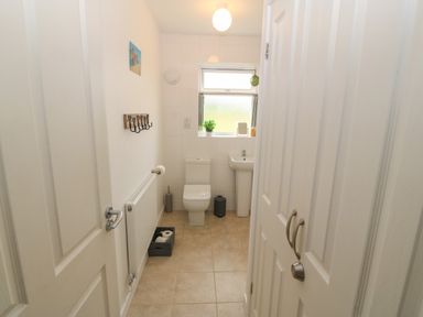 A small bathroom with a toilet sink small window and storage cabinet at Cae Berllan in Mynytho near Pwllheli