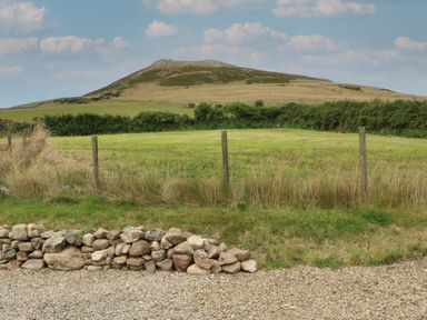 A grassy field with a hill in the background and a stone wall in the foreground at Cae Berllan in Mynytho near Pwllheli