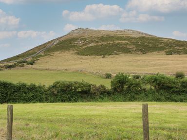 A field with a hill and stone fence under a partly cloudy sky at Cae Berllan in Mynytho near Pwllheli