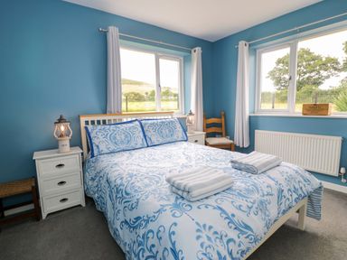 A bedroom with a double bed and windows at Cae Berllan in Mynytho near Pwllheli