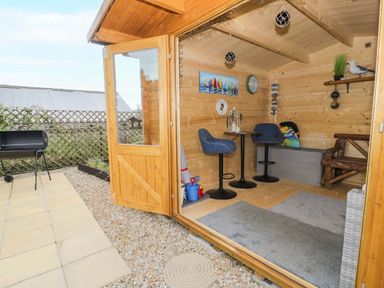 A wooden garden room with chairs and table at Cae Berllan in Mynytho near Pwllheli