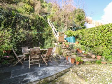 An outdoor patio with wooden table and chairs surrounded by plants and stone steps at Widgeons Keel in Flushing