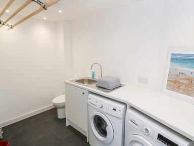 A utility room with a sink, washing machine, dryer, toilet, and a framed picture at Widgeons Keel in Flushing