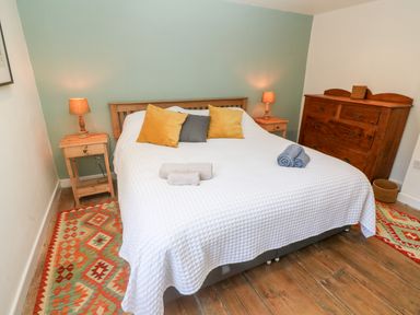 A bedroom with a bed with pillows and towels bedside tables with lamps a wooden dresser and patterned rugs at Widgeons Keel in Flushing