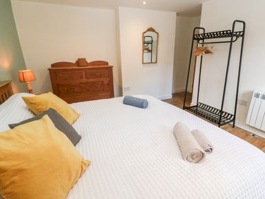 A bedroom with a bed with pillows and rolled towels a wooden dresser a floor lamp a wall mirror and a black metal clothes rack with hangers at Widgeons Keel in Flushing