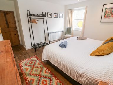 A bedroom with a bed with rolled towels and pillows a chair by the window a rack with hangers and a wooden door at Widgeons Keel Flushing