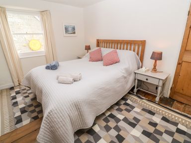 A bedroom with a bed with red checkered pillows and folded towels on top two bedside tables with lamps and a geometric patterned rug on the floor at Widgeons Keel in Flushing