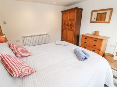 A bedroom with a bed with red checkered pillows and folded towels a wooden wardrobe a wooden chest of drawers and a mirror on the wall at Widgeons Keel in Flushing