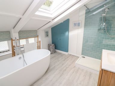 A bathroom with a freestanding bathtub shower with blue tile wall wooden cabinet and skylight at Widgeons Keel in Flushing