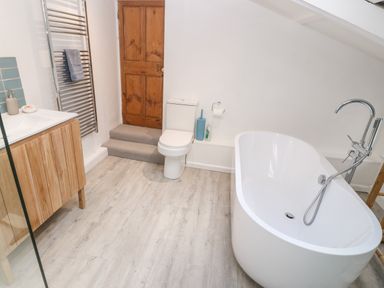 A bathroom with a freestanding bathtub toilet wooden cabinet and a wooden door at Widgeons Keel in Flushing