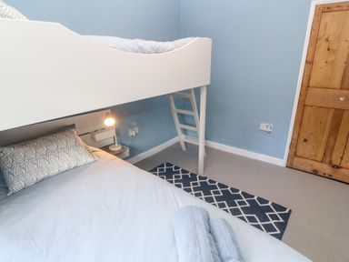A bedroom with a white bunk bed a blue patterned rug a wooden door and a bedside lamp at Widgeons Keel in Flushing