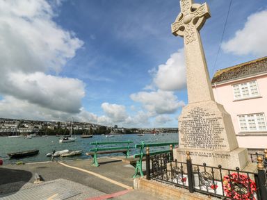 A memorial cross with inscribed names near green benches by the water with boats in view at Widgeons Keel in Flushing