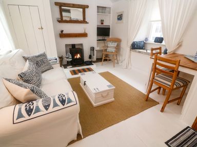 A living room with a white sofa and patterned cushions a wooden chair a fireplace and a wooden table at The Little Net Loft Mousehole near Penzance