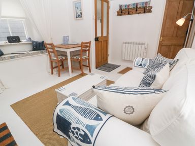 A sitting area with a white sofa and striped cushions a wooden table with two chairs and a window seat at The Little Net Loft in Mousehole near Penzance