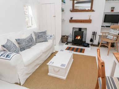 A living room with a white sofa and blue patterned cushions a white coffee table a fireplace with a wood-burning stove and a wooden chair at The Little Net Loft in Mousehole near Penzance