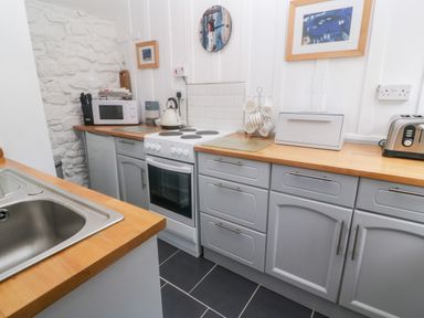 A kitchen with gray cabinets wooden countertops a white electric stove a microwave a kettle a toaster a sink and wall art at The Little Net Loft in Mousehole near Penzance