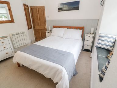 A bedroom with a double bed between two white nightstands and a wooden door at The Little Net Loft in Mousehole near Penzance