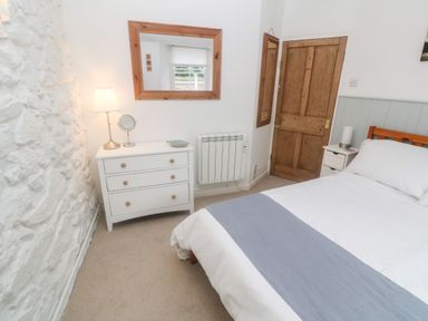 A bedroom with a bed a white chest of drawers a lamp a mirror and a wooden door at The Little Net Loft in Mousehole near Penzance