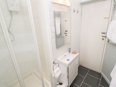 A bathroom with a shower cubicle a sink with a mirror above it a door and towel racks at The Little Net Loft in Mousehole near Penzance
