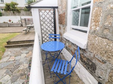 A small outdoor patio with a blue metal table and two chairs next to a stone wall at The Little Net Loft in Mousehole near Penzance