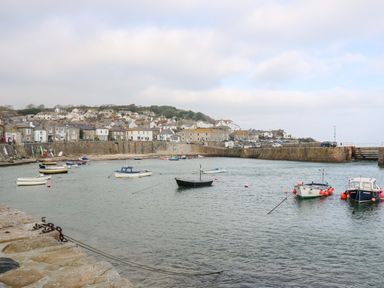 A harbor with boats on water and houses on a hill in the background at The Little Net Loft in Mousehole near Penzance