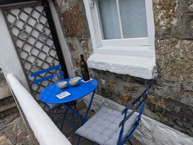 A small outdoor seating area with a blue table and chairs glasses and a bottle on the table at The Little Net Loft in Mousehole near Penzance