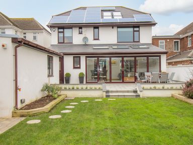 A backyard with a lawn and stepping stones leading to a patio with outdoor furniture and solar panels on the house roof at Family House in Weymouth