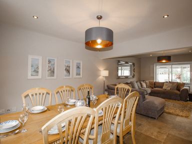A dining area with a wooden table and chairs set with plates and glasses next to a living room with a large sectional sofa and a mirror on the wall at Family House in Weymouth