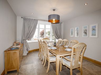 A dining room with a wooden table set for eight and a sideboard with books at Family House in Weymouth