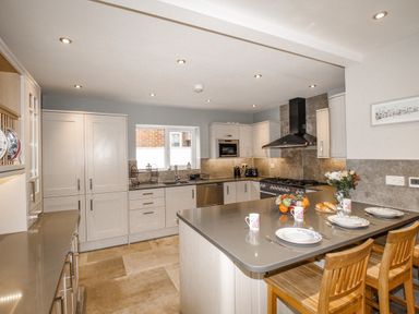 A kitchen with an island countertop set with plates and mugs and wooden chairs at Family House in Weymouth
